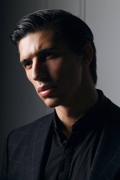 Vista lateral de um retrato close-up de um homem bonito em terno preto elegante organizar seu terno sobre fundo cinza. - Foto, Imagem