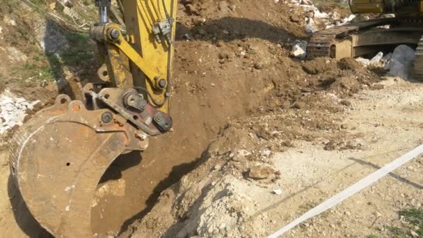 CLOSE UP: Gele graafmachine graven van een diepe sleuf in de buurt van een bouwplaats. - Video