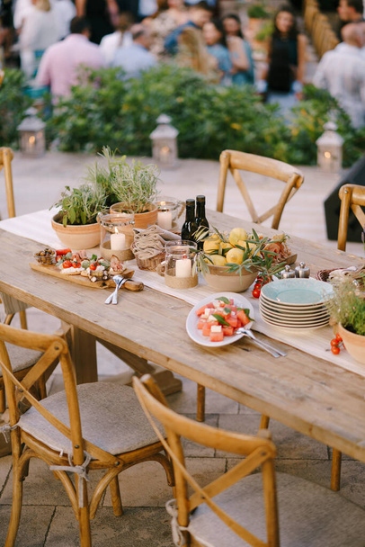 Een feestelijke tafel met verse bloemen in potten en citroenen in een diep bord in een restaurant met stoelen en gasten op een wazige achtergrond. - Foto, afbeelding