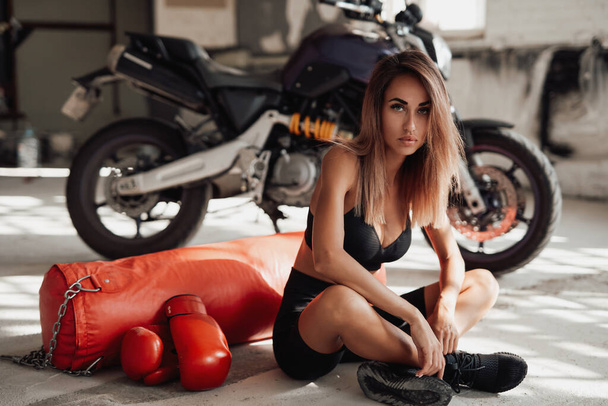 Mooi uitziende sportvrouw poseren in een studio liggend op de vloer met een bokszak. - Foto, afbeelding