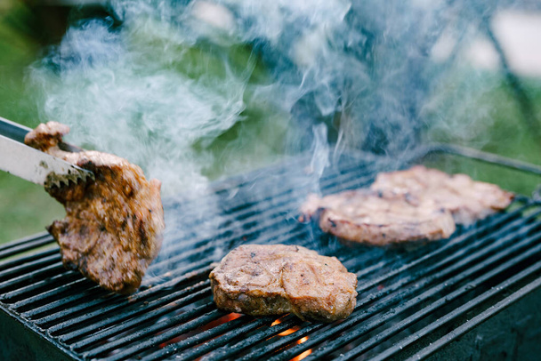 Close-up of the roasting steak on a black grill with fire and smoke. - Photo, Image