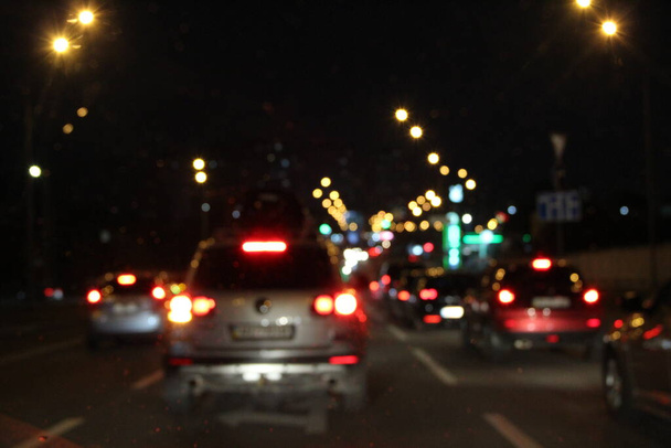 Autos mit Scheinwerfern und eingeschaltetem Licht in der nächtlichen Stadt. Autos mit eingeschaltetem Scheinwerfer. Signalbeleuchtung des Verkehrs. Schlange von Autos auf der Straße. Unscharfes Bild - Foto, Bild