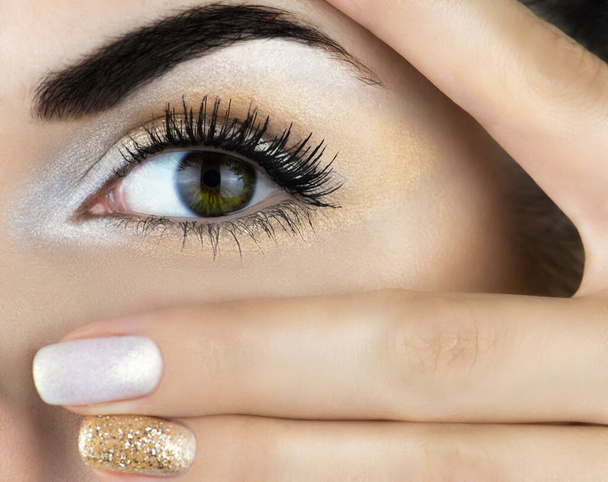 Ένα γυναικείο μάτι με χρυσό μακιγιάζ και χρυσά νύχια. Κοντινό πλάνο. - Φωτογραφία, εικόνα