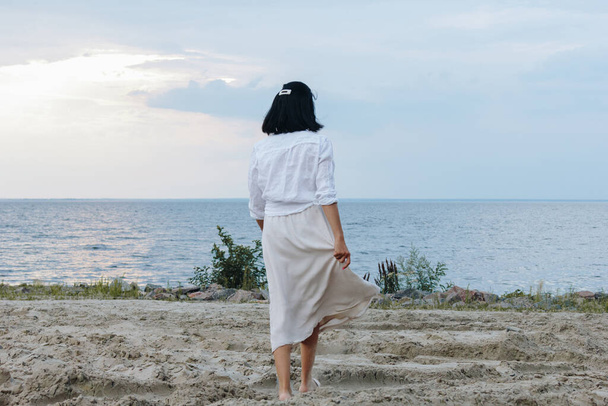 Rückansicht einer jungen Frau mit weißem Hemd und Rock am Strand - Foto, Bild