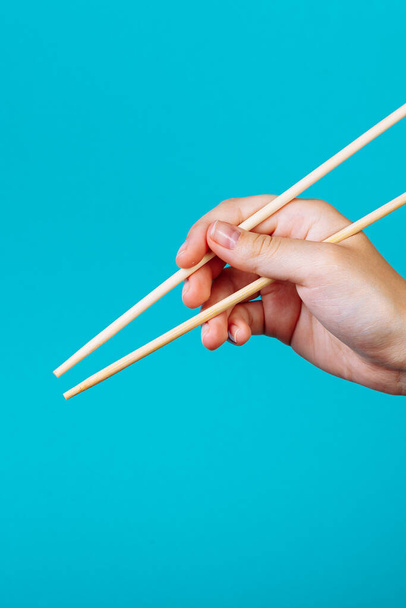 Hands holding chopsticks. Isolated on blue background, the place for caption and text. - Fotó, kép