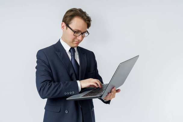 Бизнесмен держит в руках ноутбук, печатает одной рукой. Белый фон. Концепция бизнеса и финансов - Фото, изображение