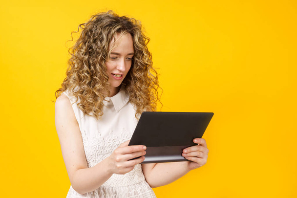 Portrait of a young woman who communicates on a tablet. Female portrait. Isolated on yellow background - Photo, Image