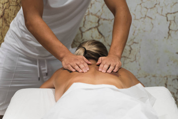 Handen van een masseur die een chiromassage behandeling toepast op de rug van een jonge vrouw met tatoeages - Foto, afbeelding