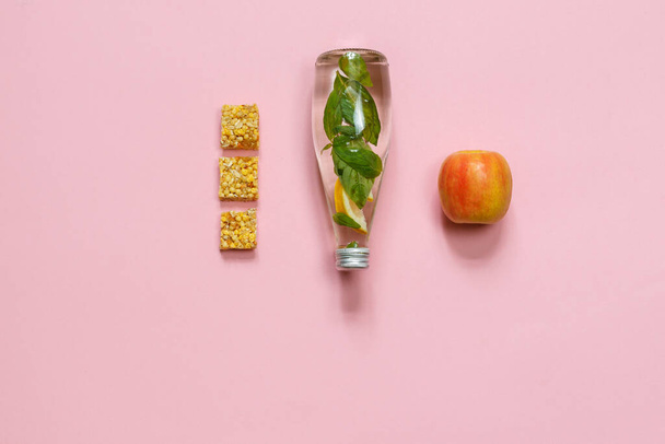 Aperitivos, una manzana, una barra de cereales y una botella de agua. Vista superior sobre fondo rosa, horizontalmente con espacio - Foto, imagen