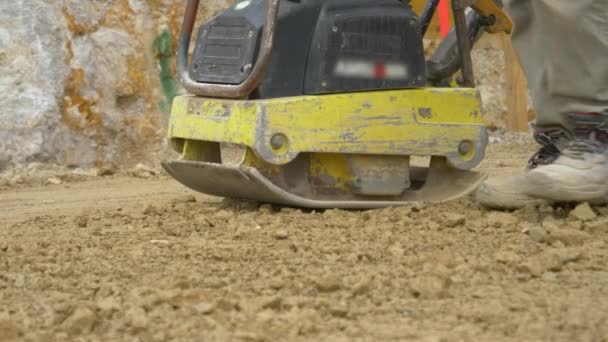 AFSLUITEN: Werknemer maakt gebruik van een egaliseermachine om grond voor betongieten voor te bereiden - Video