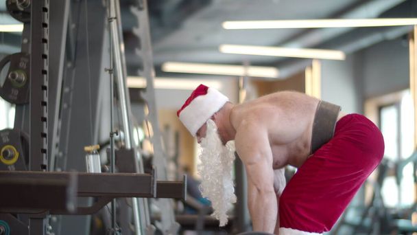 Aktiver Fitnessmann beim Kreuzheben im Fitnessstudio. Mann im Weihnachtsmannkostüm beim Workout - Foto, Bild