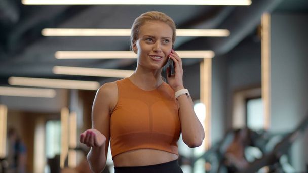 Confident athlete girl talking phone in sport club. Sportswoman standing at gym - Photo, Image