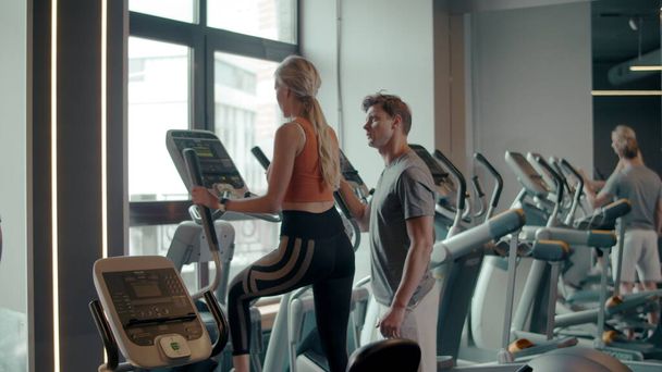 Sexy fit girl using elliptical trainer in sport club. Couple training at gym - Zdjęcie, obraz