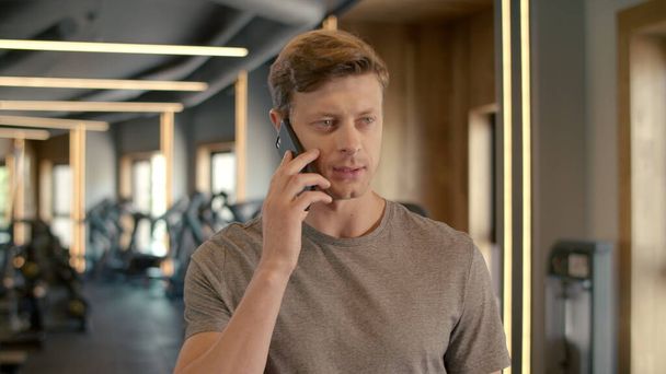 Spor kulübünde telefonda konuşan yakışıklı bir sporcu. Vücut geliştirici spor salonunda duruyor.. - Fotoğraf, Görsel