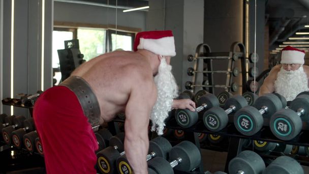 Papai Noel fazendo roubos de halteres no ginásio. Esportista treino no clube desportivo
 - Foto, Imagem