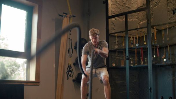 Deportista fuerte usando cuerdas de batalla en el gimnasio. Entrenamiento de hombre en gimnasio
 - Foto, imagen