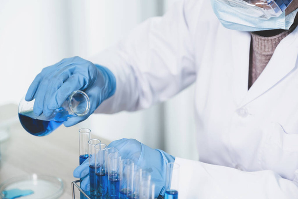 Οι επιστήμονες χέρι κρατήστε ένα ποτήρι γεμάτο με μπλε χημικό υγρό για έρευνα και ανάλυση σε ένα εργαστήριο. - Φωτογραφία, εικόνα