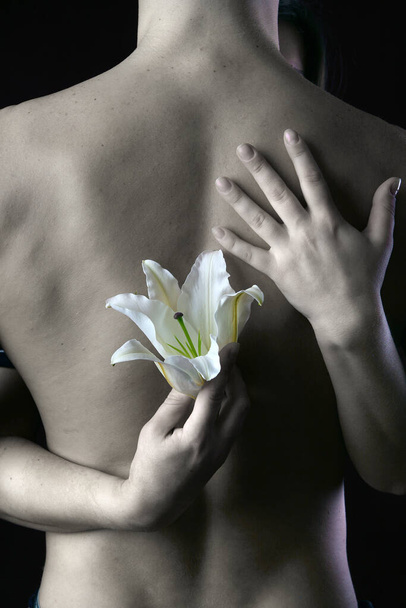 close-up delicate white lily in the hands against the background of naked torso, studio dark background - Fotoğraf, Görsel