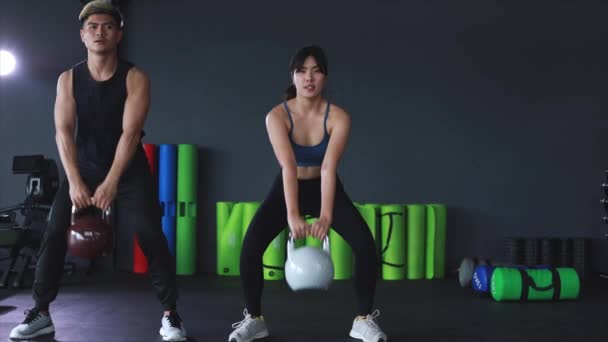 Images de l'homme et la femme asiatique faisant kettlebell swing exercice ensemble à la salle de gym. - Séquence, vidéo