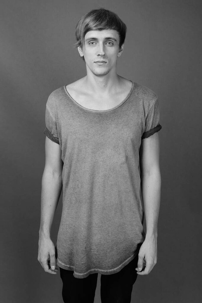 Estudio de hombre guapo joven con el pelo rubio sobre fondo gris en blanco y negro - Foto, imagen