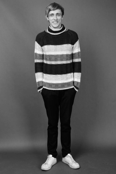 Studio shot van jonge knappe man dragen coltrui tegen grijze achtergrond in zwart-wit - Foto, afbeelding