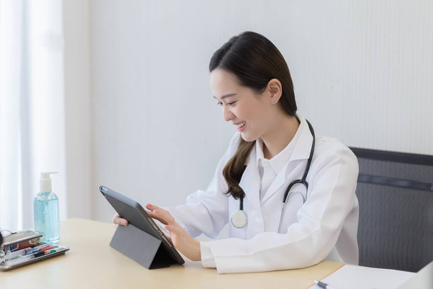 Лікар азіатської жінки шукає інформацію про пацієнта на її планшеті з щасливим обличчям в офісі лікарні.. - Фото, зображення