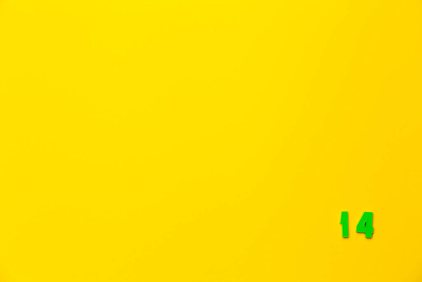 A green plastic toy number fourteen is located in the lower right corner on a yellow background. - Photo, Image