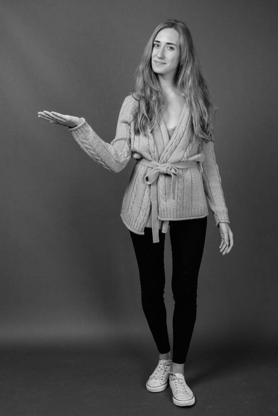 Studio colpo di giovane bella donna con i capelli biondi indossa abiti caldi contro sfondo grigio in bianco e nero - Foto, immagini