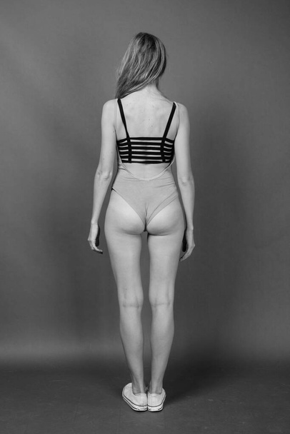 Studio shot of young beautiful woman with blond hair wearing leotard against gray background in black and white - Φωτογραφία, εικόνα