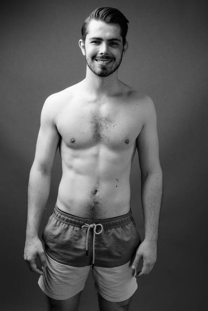 Studio shot of young handsome bearded man shirtless against gray background in black and white - Foto, Imagen