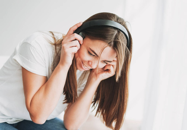 Portrait of smiling young woman brown hair and green eyes with freckles in white t-shirt and jeans listening music by headphones - Valokuva, kuva