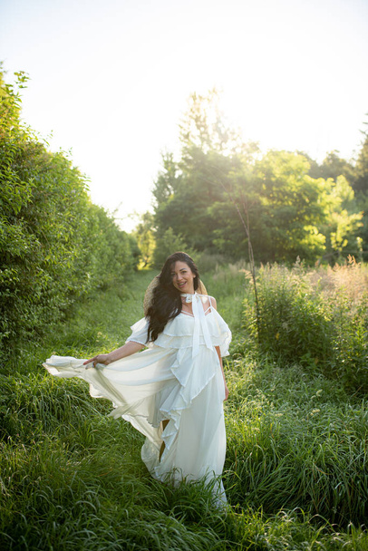 Kobieta w ciąży pozowanie w białej sukience na tle natury. - Zdjęcie, obraz