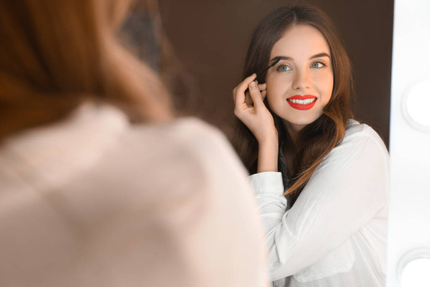 Young woman doing makeup near mirror in dressing room - Foto, Imagem