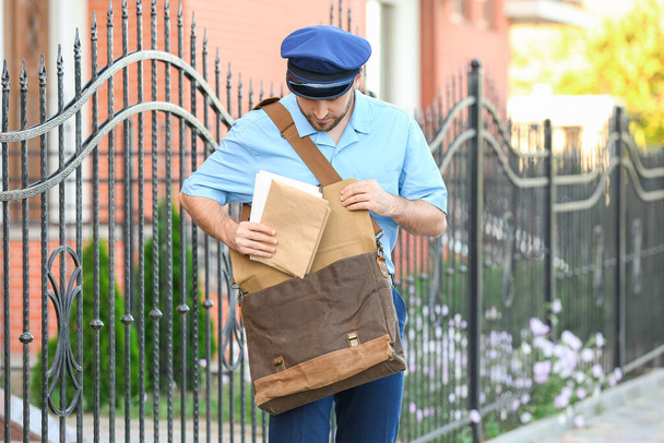 Красивый молодой почтальон с письмами на улице - Фото, изображение
