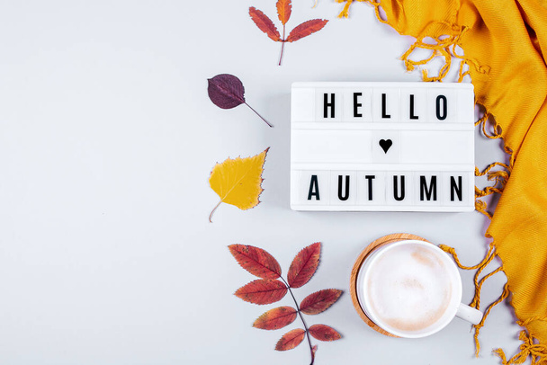 Cup of coffee, orange scafr and light box with words Hello Autumn and Colorful autumn fall leaves on grey background. Flat lay - Foto, Imagem