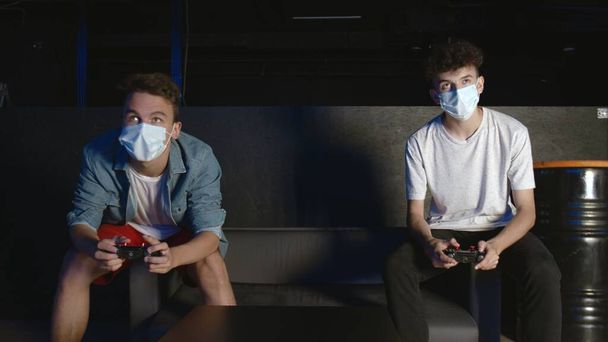 Zwei Spieler mit Gesichtsmasken vor dem Bildschirm spielen gemeinsam in der Online-Schlacht - Foto, Bild