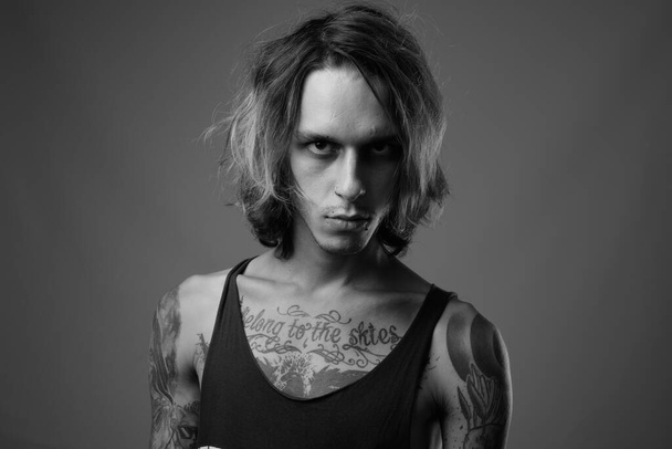 Estudio de un joven rebelde con tatuajes corporales sobre fondo gris en blanco y negro - Foto, imagen