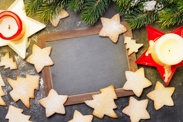 Carte de voeux de Noël avec sapin, biscuits au pain d'épice et bougies sur fond de pierre. Vue de dessus plat avec tableau noir pour vos salutations de Noël - Photo, image