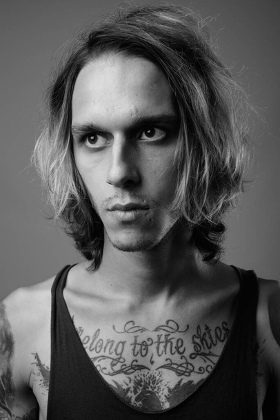 Студійний знімок бунтівного молодого чоловіка з татуюванням на тілі на сірому фоні в чорно-білому
 - Фото, зображення