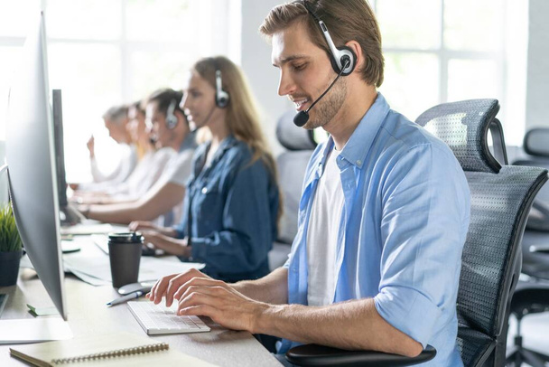 Mladý pohledný muž zákaznické podpory telefonní operátor se sluchátky pracuje v call centru - Fotografie, Obrázek