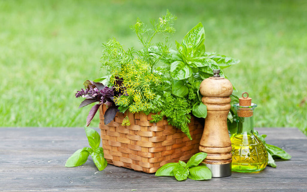 Varias hierbas en cesta, aceite de oliva y pimienta en la mesa de jardín - Foto, Imagen