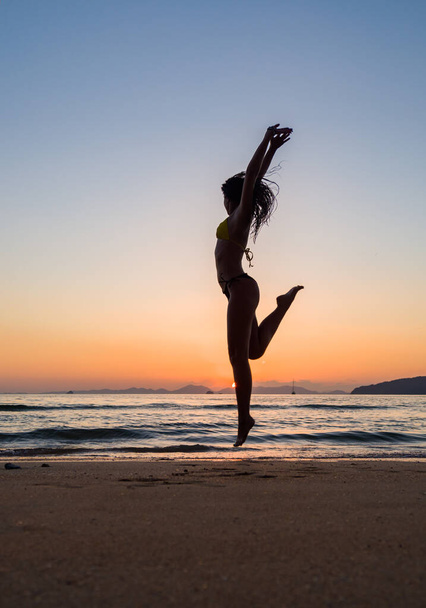 Woman in swiming suit jumping on the beach at sunset - 写真・画像