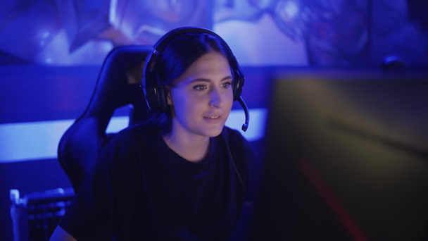 Młoda kobieta siedzi w słuchawkach w nowoczesnym klubie komputerowym, gra w grę online. Kobieta uśmiecha się i jest zaskoczona grą internetową. Widok na portret. - Zdjęcie, obraz