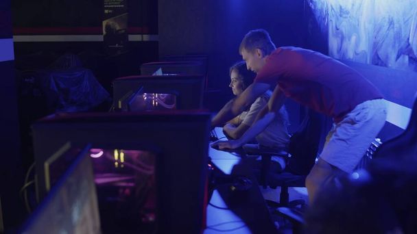 Junger Mann hilft seiner Freundin bei Sieg in Shooter-Videospiel in modernem Cybersport-Club - Foto, Bild