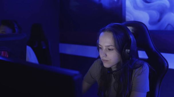 Young woman sits in headphones at a modern computer club, plays an online game. Woman smiles and is surprised at the internet game. Portrait view. - Фото, зображення