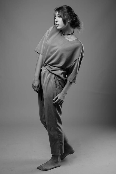 Studio shot of young beautiful woman wearing matching clothes against gray background in black and white - Foto, Imagen