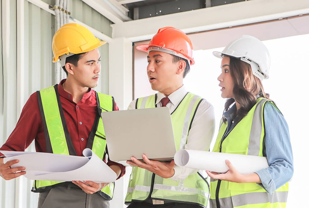 Portrait de trois équipes de construction confiantes, une femme architecte et deux ingénieurs, portant des casques de sécurité, tenant un ordinateur et du papier bleu, discutant du projet sur le chantier. - Photo, image