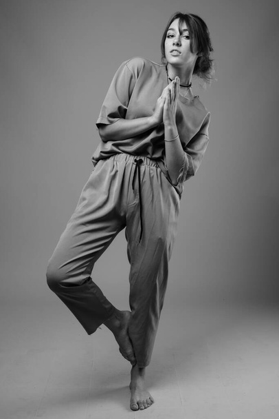 Studio shot van jonge mooie vrouw dragen bijpassende kleding tegen grijze achtergrond in zwart-wit - Foto, afbeelding