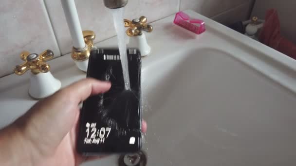 lavare a mano il telefono cellulare sotto l'acqua del rubinetto contro covid 19, coronavirus e batteri - Filmati, video