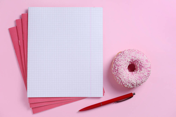 Cuadernos escolares y rosquilla rosa sobre fondo de color, vista superior - Foto, imagen